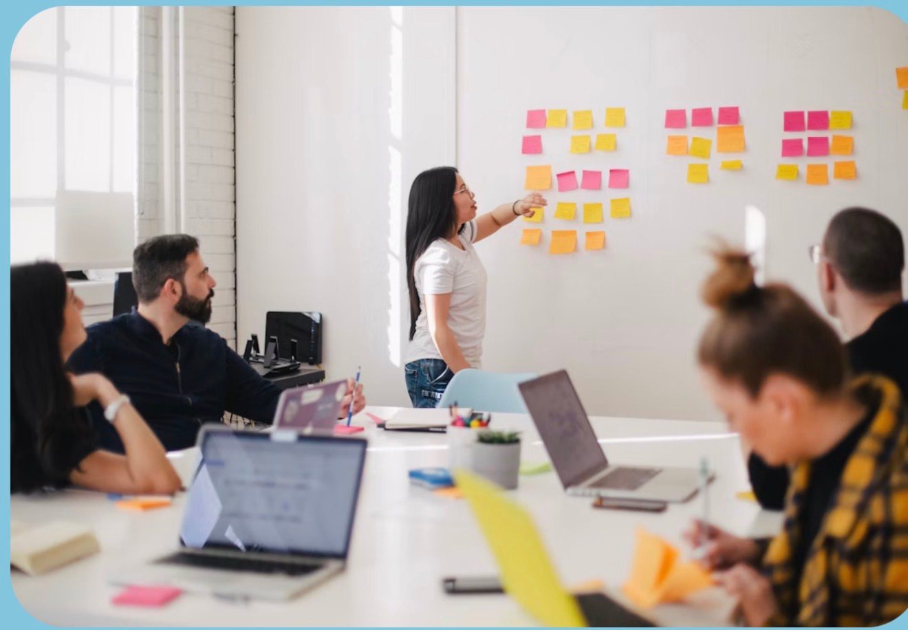 A structured sticky-note matrix being worked on a wall mid-session: a woman at the board grouping coloured notes into columns